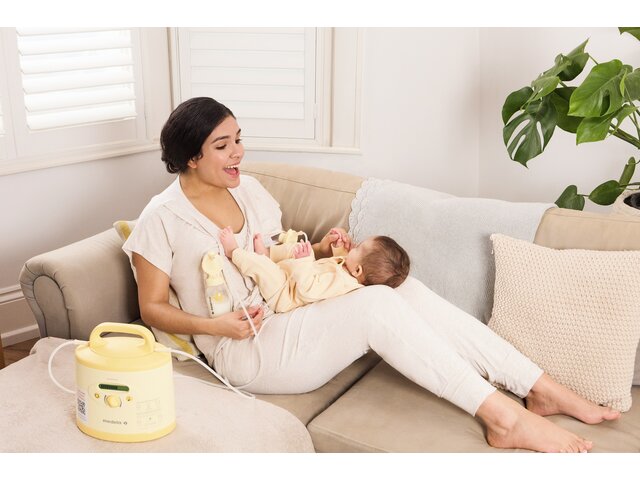 A mom plays with her baby on her lap while lying on the couch and pumping with her rented Medela Symphony PLUS® breast pump.
