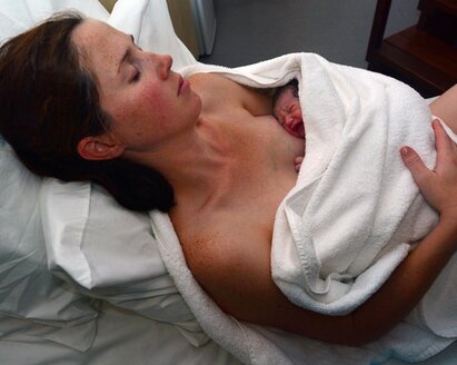 Eine Mutter hält ihr in ein Handtuch gewickeltes Baby unmittelbar nach der Geburt.