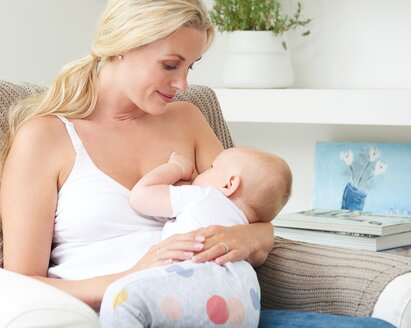 Eine Mutter sitzt zu Hause auf einem Stuhl und stillt ihr Baby.