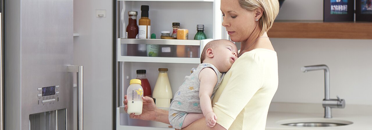 Une maman tient son bébé dans la cuisine pendant qu'elle prépare du lait exprimé réfrigéré pour une tétée.