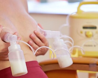Frau sitzt auf einem Stuhl und pumpt mit einer Medela Symphony Milchpumpe ab.